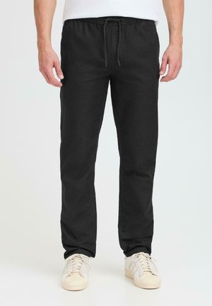 Black trousers with an elastic waistband and drawstring, featuring a straight cut and smooth cotton fabric. Paired with white sneakers.
