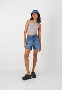Šedý halter top, riflové šortky a čierne platformové klobúky. Krátke vlasy, má na sebe modro-biely vedierkový klobúk s rozstrapkaným okrajom.