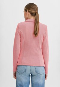 Rosa blazer med en texturerad yta, skräddarsydd passform och detaljer med slits baktill, kombinerad med ljusblå jeans. Enkel kragsdesign med långa ärmar.