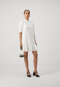 Vit kortärmad klänning med krage, strukturerad tyg, volangkant och spetsdetaljer. Matchad med en svartvit pärlhandväska.