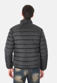 Giacca a vento nera con design a righe orizzontali, caratterizzata da un colletto alto e una texture liscia e lucida, indossata sopra jeans blu.