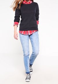 Marinblå strukturerad stickad tröja över en röd rutig skjorta, kombinerad med ljusblå jeans och svart-vita sneakers. Slim fit-design.