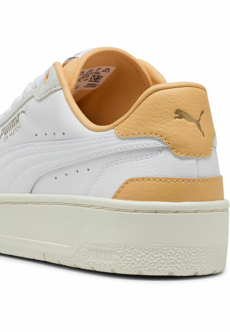 Weiße Leder-Sneaker mit einem sandfarbenen Akzent an der Ferse, goldenem Logo, strukturiertem Profil und durchbrochener Detailgestaltung für Atmungsaktivität.
