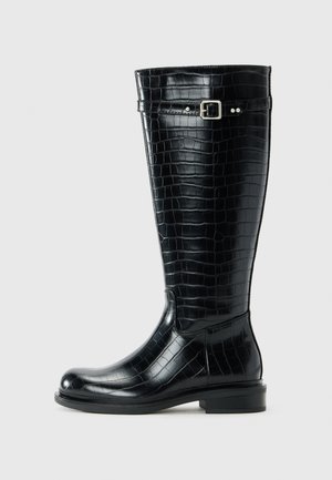 Botte noire hauteur genou avec texture crocodile, bout rond, petit talon carré et une sangle à boucle argentée près du haut.