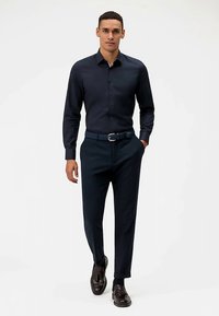 Donkerblauw overhemd met knopen en lange mouwen, gecombineerd met donkerblauwe, op maat gemaakte broek en bruine leren loafers. Slanke pasvorm, gladde textuur.