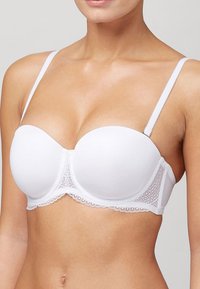 Witte straploze beha van gladde stof, met gepatte cups en delicate kanten rand langs de onderkant. Aanpasbare bandjes zijn aanwezig.