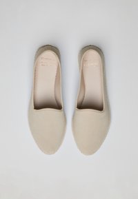Beige Slipper mit einer weichen Wildleder-Oberfläche, runder Zehenform und gesteppten Details um die Sohle. Das Innere weist eine geprägte Markenkennzeichnung auf.