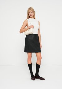 Top alb cu dungi, fără mâneci, fustă mini din piele neagră, ciorapi negri până la genunchi și loafers burgundy. Geantă mică crem cu accente aurii.