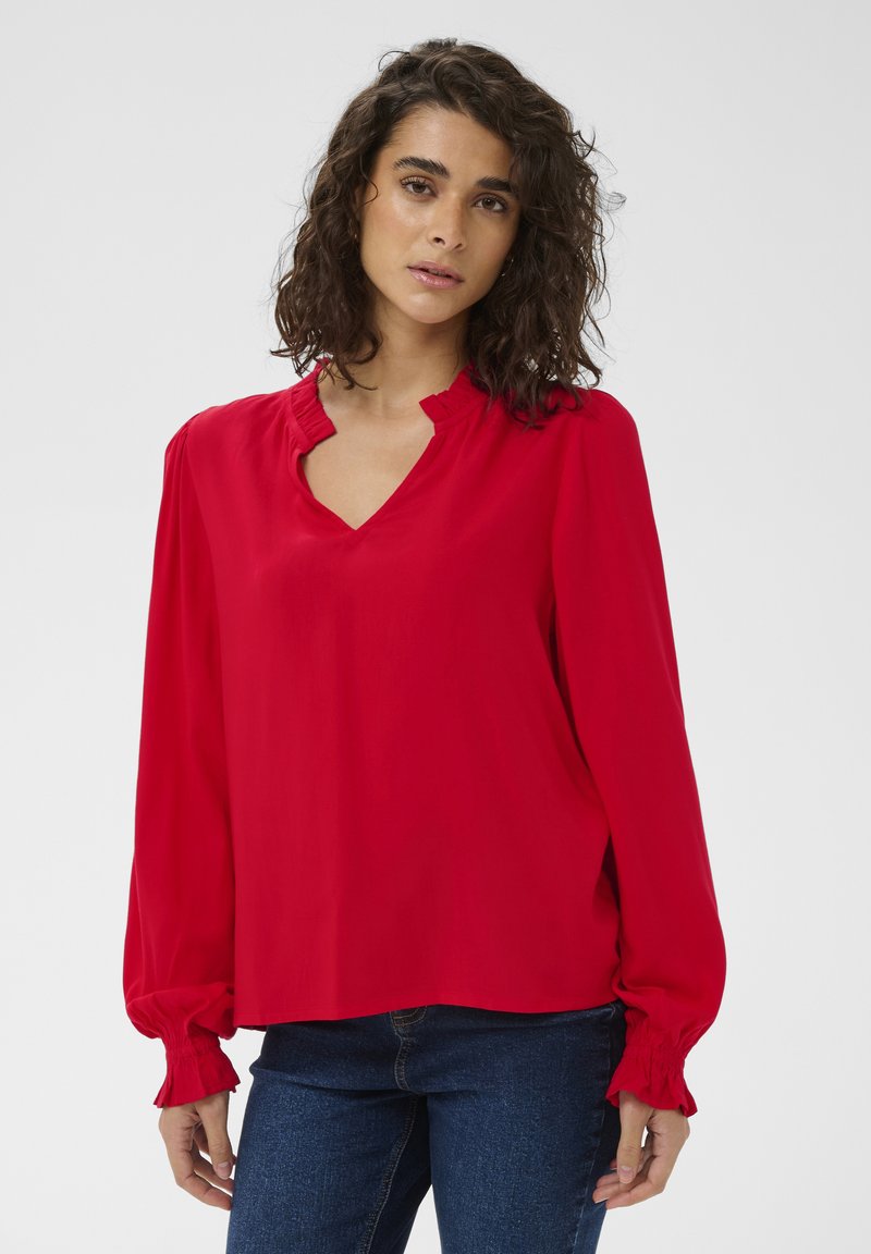 Blouse rouge avec un col en V et un col à volants, manches longues avec poignets froncés, tissu lisse et coupe décontractée.