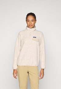 Fleece-Pullover in hellem Beige mit strukturiertem Muster, hohem Kragen und einer Druckknopftasche auf der Brust. Weicher Stoff mit entspannter Passform.