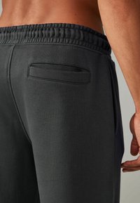 Donkergrijze sweatpants met een tailleband met trekkoord, een gladde textuur en een klein achterzakje met een nette naaddetail.