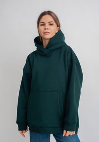 Overmaat groene capuchontrui van zachte stof, met een grote kangoeroezak en geribde manchetten in een relaxte pasvorm.