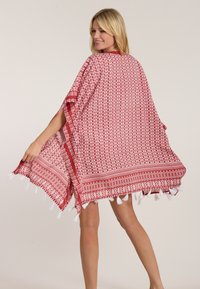 Sarkana un baltā rakstota kaftāna ar pušķu akcentiem, brīvs piegriezums, īsas piedurknes, viegla auduma un simetrisku ģeometrisku dizainu.