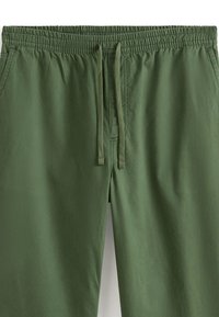 Zielone, lekkie spodnie z elastycznym pasem i sznurkiem. Gładka tekstura z przeszytymi szwami i bez widocznych kieszeni.