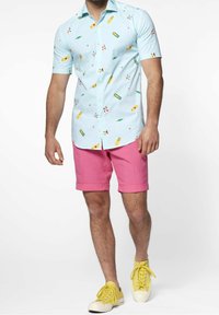 Camicia azzurra a maniche corte con motivi colorati, abbinata a pantaloni corti rosa. Il modello indossa sneaker gialle. Tessuto morbido, vestibilità casual.