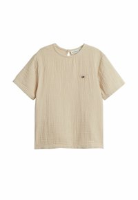 Beige bomullströja med en texturerad yta, korta ärmar och en liten broderad design på bröstet. Detalj med nyckelhål på baksidan.