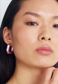 Pink geometric acrylic earrings with a shiny finish, featuring a bold, angular design. Worn on a smooth, clear-skinned model.