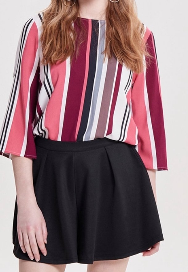 Femme portant un chemisier à rayures verticales rose, blanc, noir, violet et gris avec des manches trois-quarts et une jupe noire évasée.