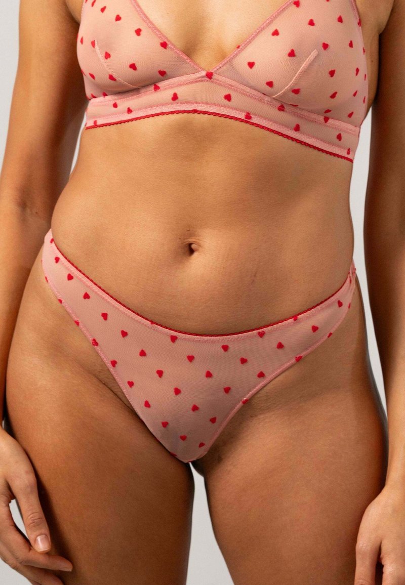 Rosa nätlingerie-set med en bh och tanga, dekorerad med små röda hjärtan och avslutad med kontrasterande röd kant.