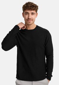 Zwarte langekous T-shirt van een gladde, lichte stof met een ronde hals, aansluitende mouwen en een subtiele textuur.