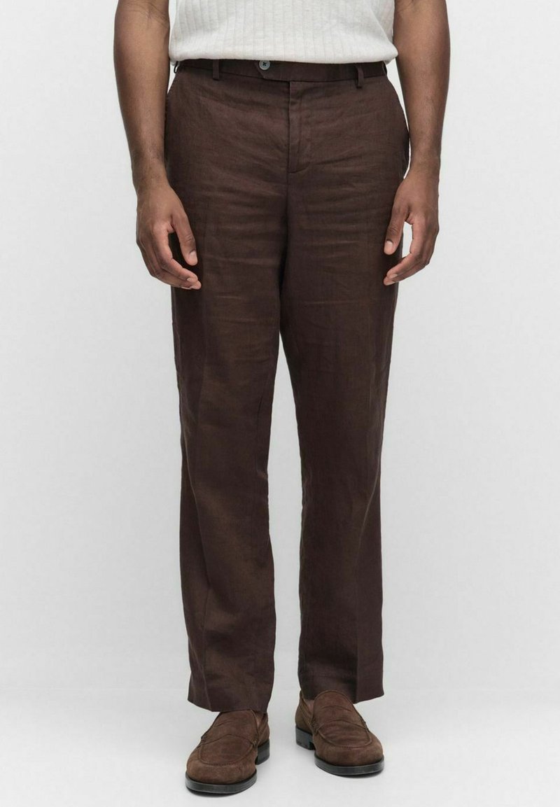 Bruna linbyxor med rak benform, med midjeband och subtil textur. Kompletteras av mörkbruna skor.