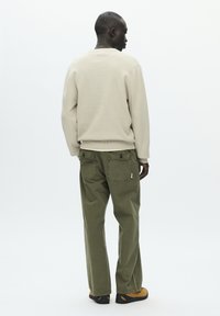 Pull beige avec ourlet côtelé, associé à un pantalon ample vert olive avec détail de poche. Le mannequin porte des chaussures marron et noires.