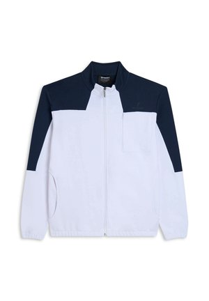 Veste blanche zippée avec des panneaux supérieurs bleu marine. Comprend un col montant, des poches latérales et une poche poitrine. Fabriquée en tissu doux.