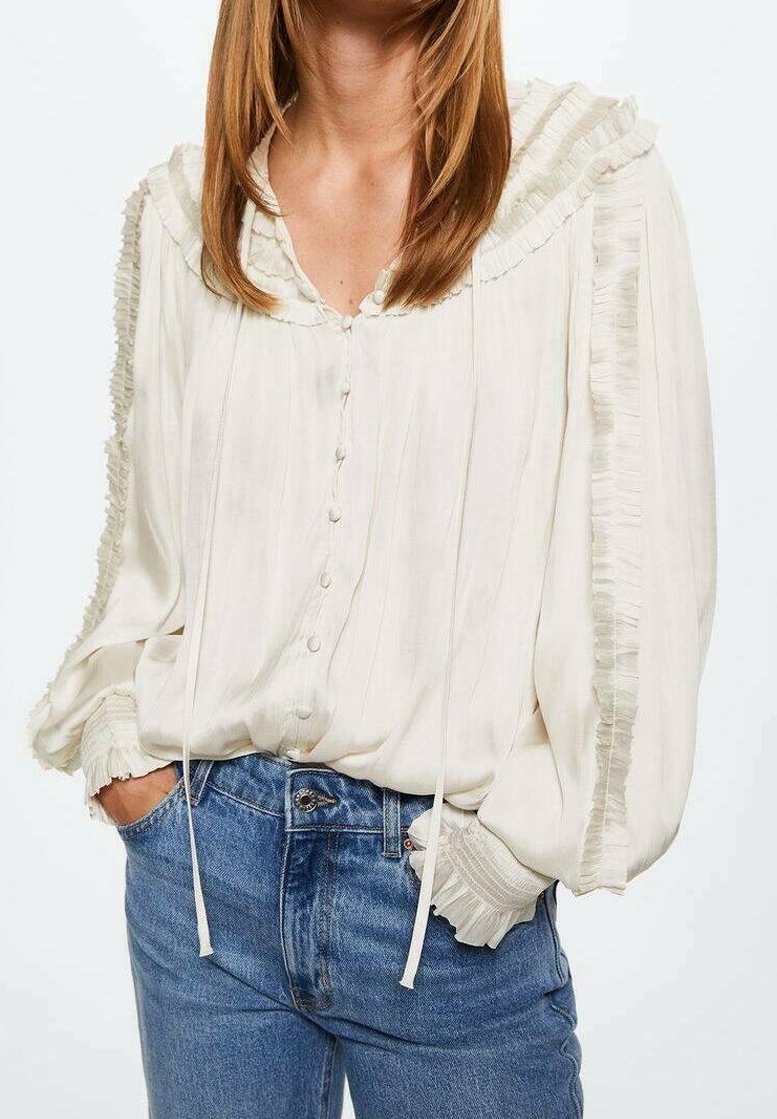 Witte blouse met een gerimpelde kraag en textuurmouwen, voorzien van een knoopsluiting en trekkoordaccenten. G gedragen met blauwe denim jeans.