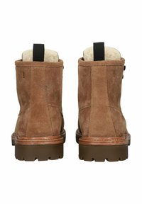 Botas de tobillo de ante marrón con forro de felpa, suela moldeada y lengüeta en la parte trasera. Presenta costuras simples y detalles de botones en los laterales.