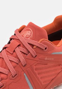 Röd vandrarsko med en texturerad, syntetisk ovandel, med en gummisula, GORE-TEX-logotyp och texturerade detaljer på sidorna.