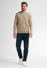 Beżowy sweter o splocie z okrągłym dekoltem, z fakturowanym wzorem, w połączeniu z ciemnoniebieskimi dżinsami i białymi trampkami. Dyskretny logo na swetrze.