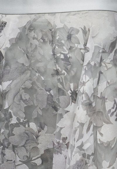 Διάφανο λευκό ύφασμα με περίτεχνα γκρι λουλουδάτα σχέδια που δημιουργούν ένα στρωματοποιημένο, υφασματικό εφέ.