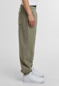 Pantaloni de trening verde măsliniu cu talie elastică, buzunar lateral, manșete conice și detalii fine de cusătură, asortați cu adidași albi.