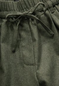 Pantalons en tissu texturé vert olive avec taille élastique et cordon de serrage. Comprend une poche latérale et une coupe douce et décontractée.