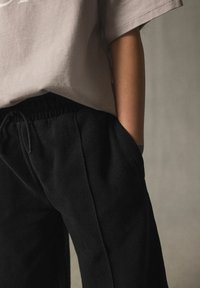 Graues T-Shirt mit kurzen Ärmeln, kombiniert mit schwarzen Jogginghosen mit elastischem Bund und seitlichen Taschen, aus einem weichen, strukturierten Stoff.