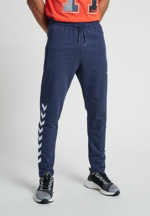 Jogging en navy avec une finition texturée, dotés d'une taille à cordon, de poches zippées et d'un motif chevron blanc sur le côté.