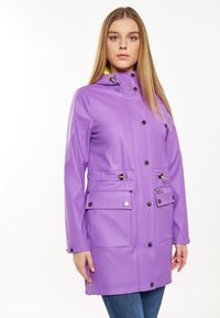 Fioletowy wodoodporny płaszcz z kapturem, z zatrzaskami, dwiema dużymi kieszeniami i detalami w postaci zapięcia typu toggle. Gładkie, błyszczące wykończenie, o długości sięgającej kostek.
