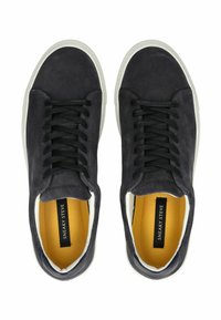 Schwarze Wildleder-Sneaker mit weißen Gummi-Sohlen, ausgestattet mit schwarzen Schnürsenkeln und einem kontrastierenden gelben Innenfutter. Minimalistisches Design, runde Zehenform.