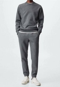 Grå sweatshirt og matchende joggingbukser lavet af et blødt stof, med rund halsudskæring, elastiske manchetter og sidelommer. Båret med hvide sneakers.