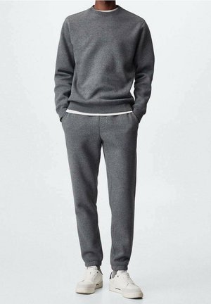 Grå sweatshirt og matchende joggingbukser lavet af et blødt stof, med rund halsudskæring, elastiske manchetter og sidelommer. Båret med hvide sneakers.