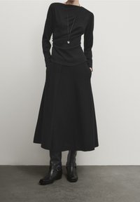 Black long-sleeve top with a sleek design, paired with a flowing black skirt. Black leather ankle boots with buckle accents complete the look.