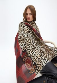 Leopardprint sjal med et rødt ternet mønster, der har et prydet emblem detalje; blødt stof draperet over en model.