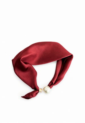 Czerwona jedwabna chusta z ozdobnym złotem i dużą perłopodobną koraliką na końcach, ułożona w pętlę na białym tle.