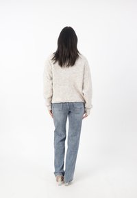 Ljusbeige fluffig tröja i avslappnad passform; i kombination med ljusblå raka jeans och klara klackskor. Sedd bakifrån.