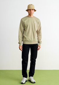 Beige sweatshirts med logo, sorte bukser og en lys beige bøttehat. Båret med grå sneakers. Simpelt design, afslappet pasform, glat tekstur.