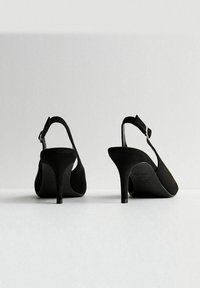 Tacchi slingback in suede nero con punta affilata e tacco a stiletto di 3 pollici, caratterizzati da una fascia alla caviglia e lati aperti. Suola piatta.