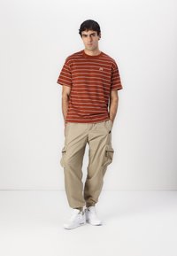 Rød- og hvidstribet kortærmet t-shirt parret med beige cargo bukser med sidelommer og hvide sneakers med en tekstureret sål.