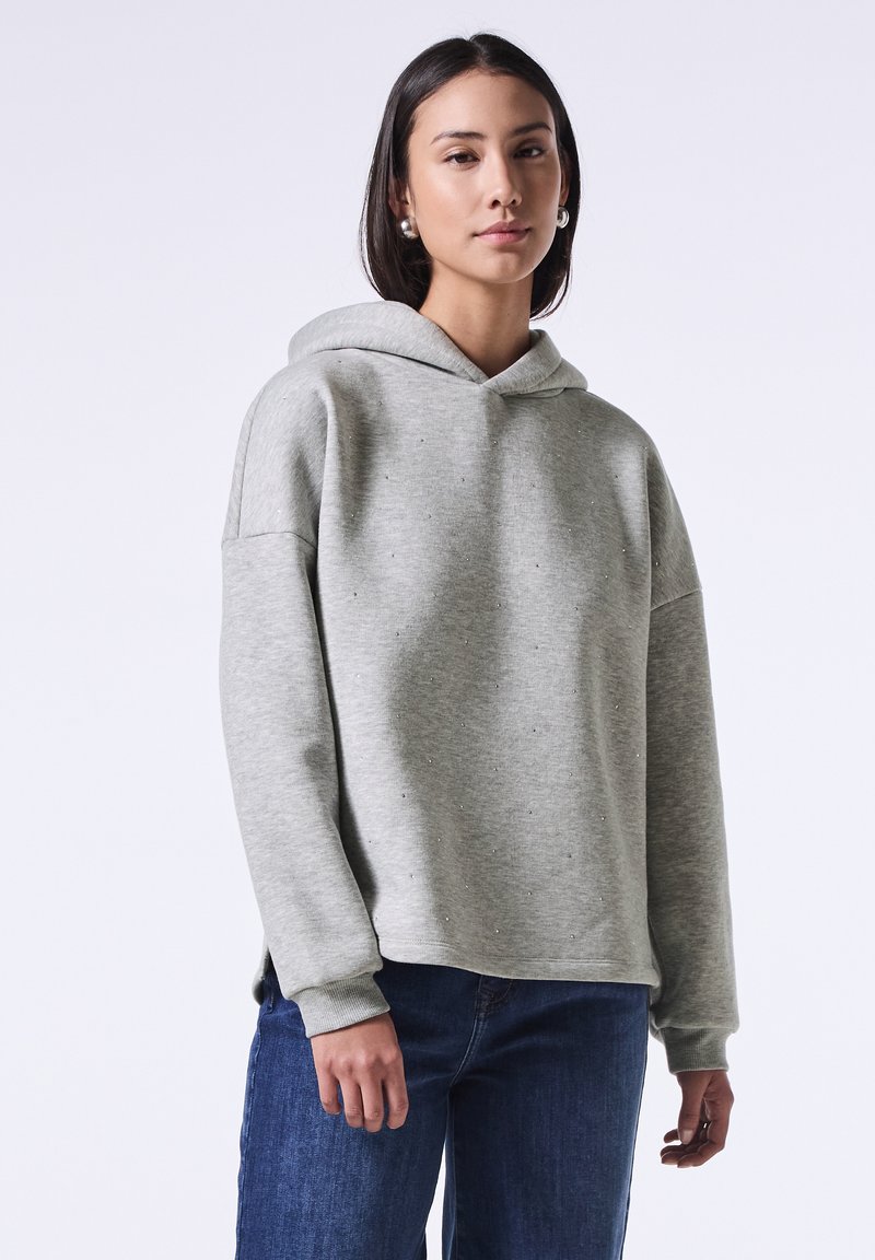 Sudadera gris claro con un corte relajado, textura suave y acentos de rhinestone dispersos, combinada con jeans azul oscuro.
