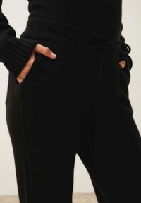 Svarta stickade loungbyxor med dragsko i midjan, ribbade muddar och sidofickor. Mjuk textur med en strömlinjeformad silhuett.