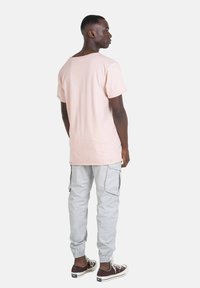 Camiseta de algodón rosa claro, corte relajado, combinada con pantalones cargo gris claro con bolsillos laterales y zapatillas marrones con suelas blancas.